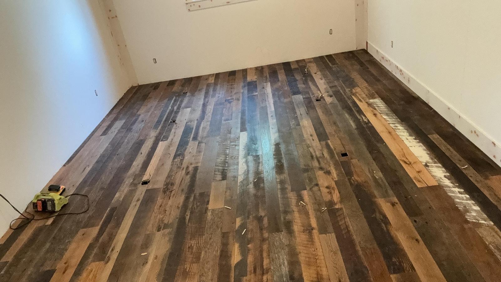 Reclaimed plank hardwood flooring mid-install with tools on the floor
