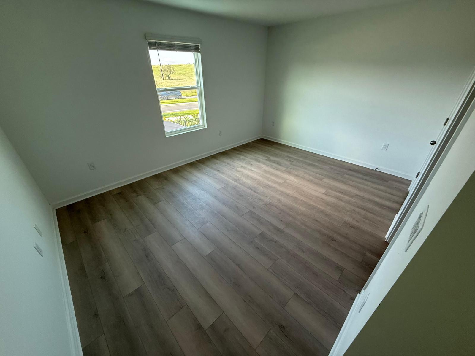Grey-brown LVP plank in a residential bedroom with a window overlooking the road