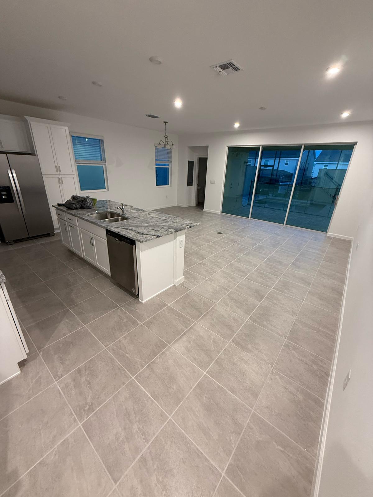Open-plan kitchen and great room with large-format grey tile flooring and granite island