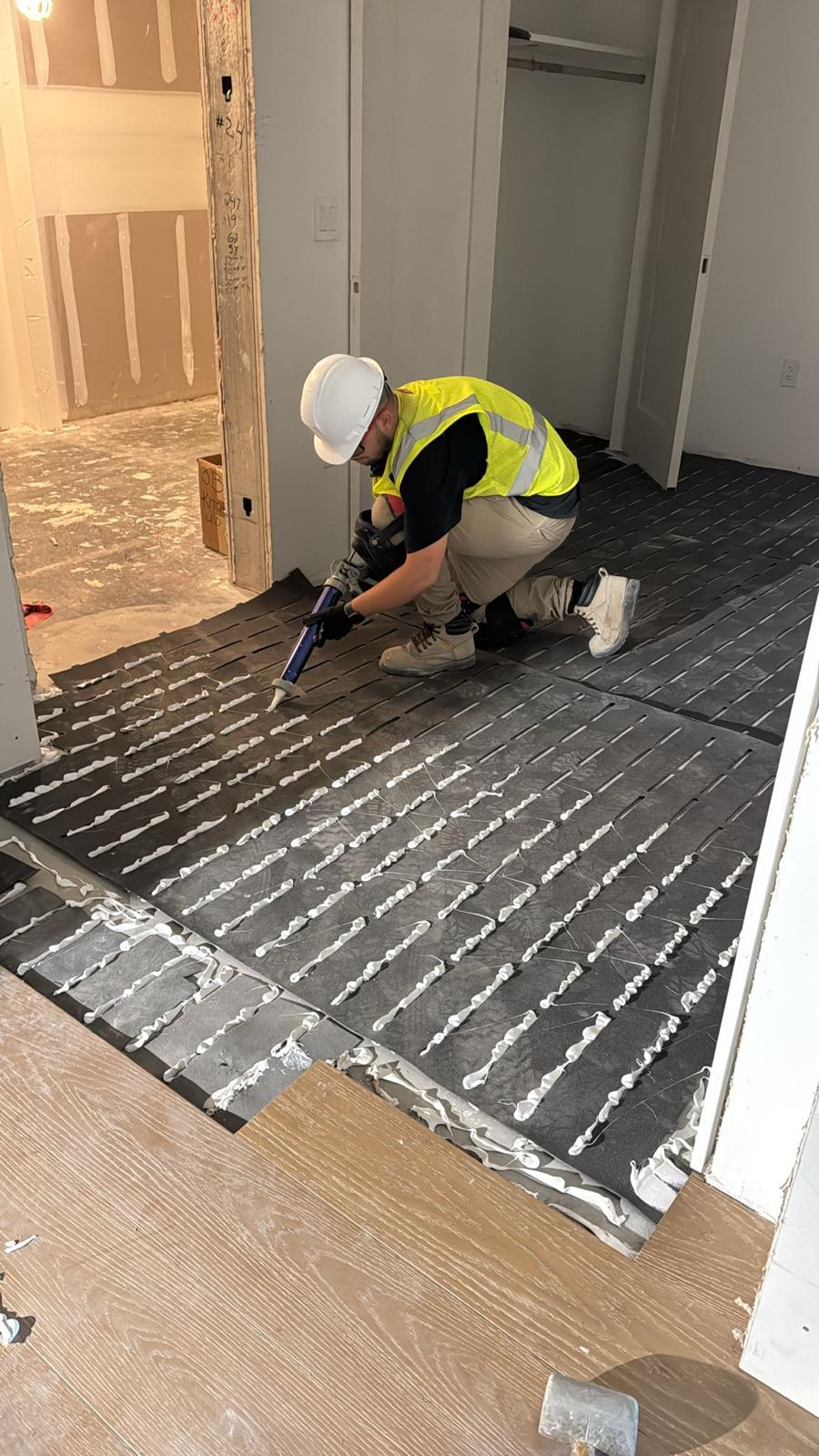 4You Flooring installer in hi-vis vest and hard hat applying adhesive over acoustic underlayment