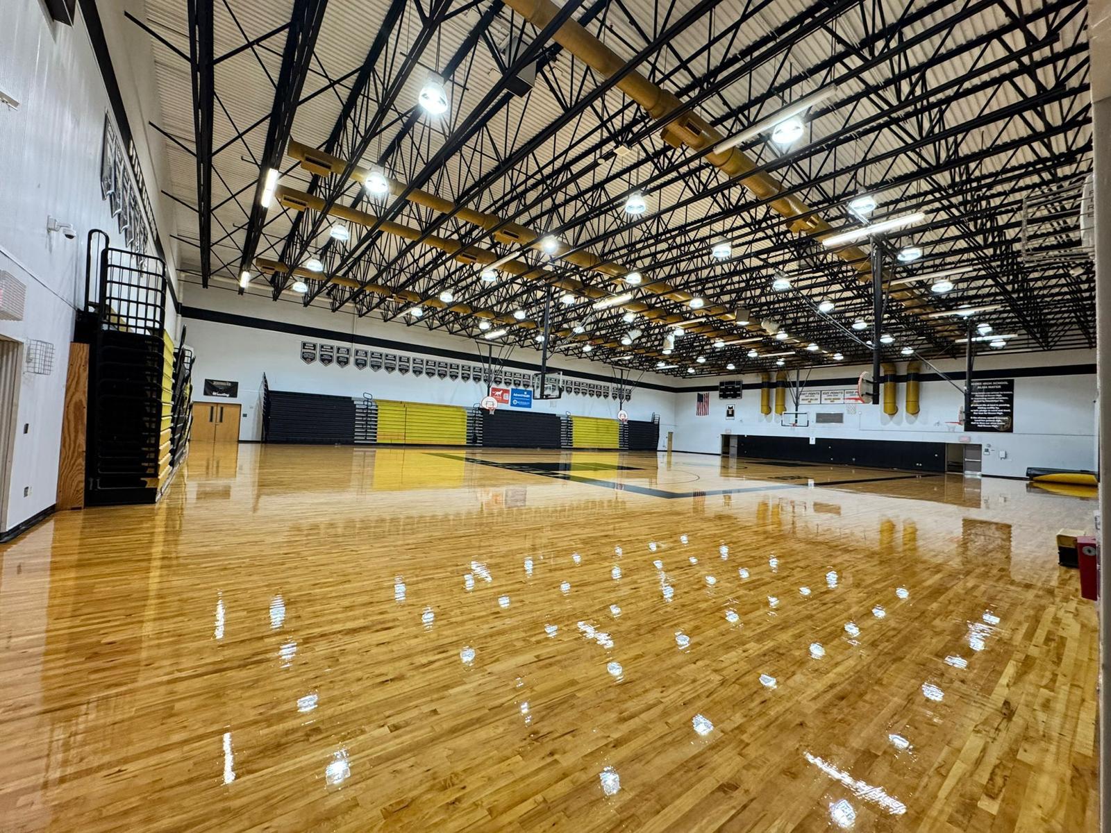 Refinished maple high-school gymnasium floor with yellow and black trim and fold-out bleachers